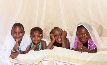 Young girls in Senegal lie in bed under a mosquito net.